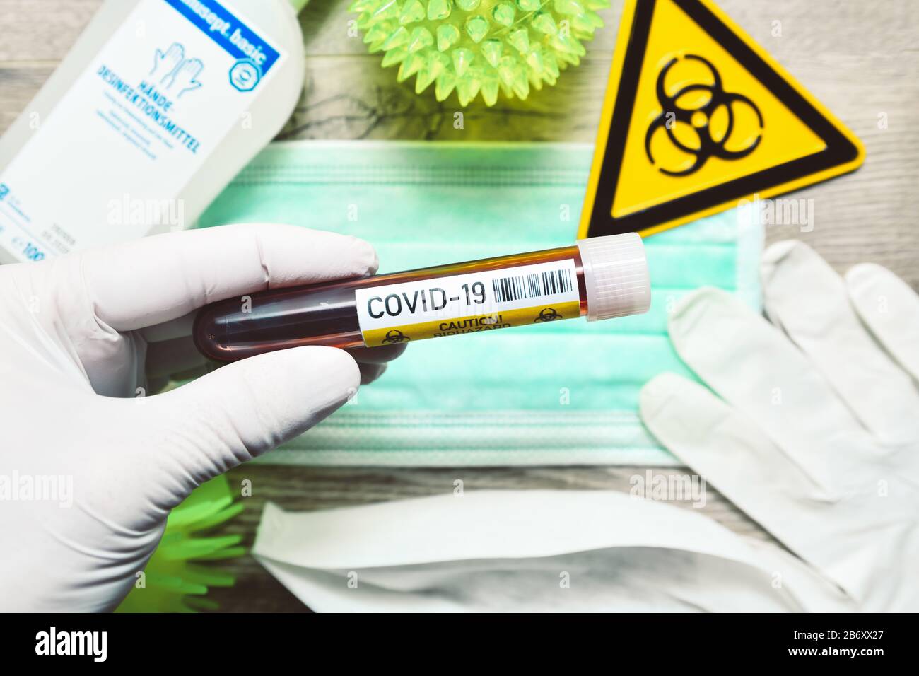 Main im Latexhandschuh haelt Blutentnahmeroehrchen vor einem Mundschutz, Symbolfoto Coronavirus Banque D'Images