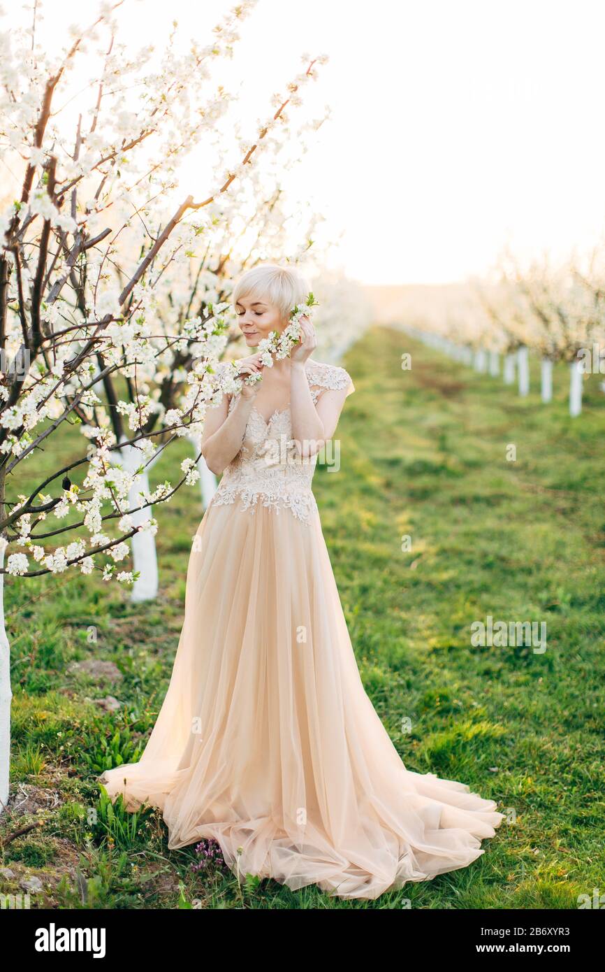 Belle mariée dans une robe longue et élégante orange clair, se posant à  l'extérieur dans le jardin fleuri de fruits, odorant l'arôme des fleurs sur  la branche d'arbre Photo Stock - Alamy