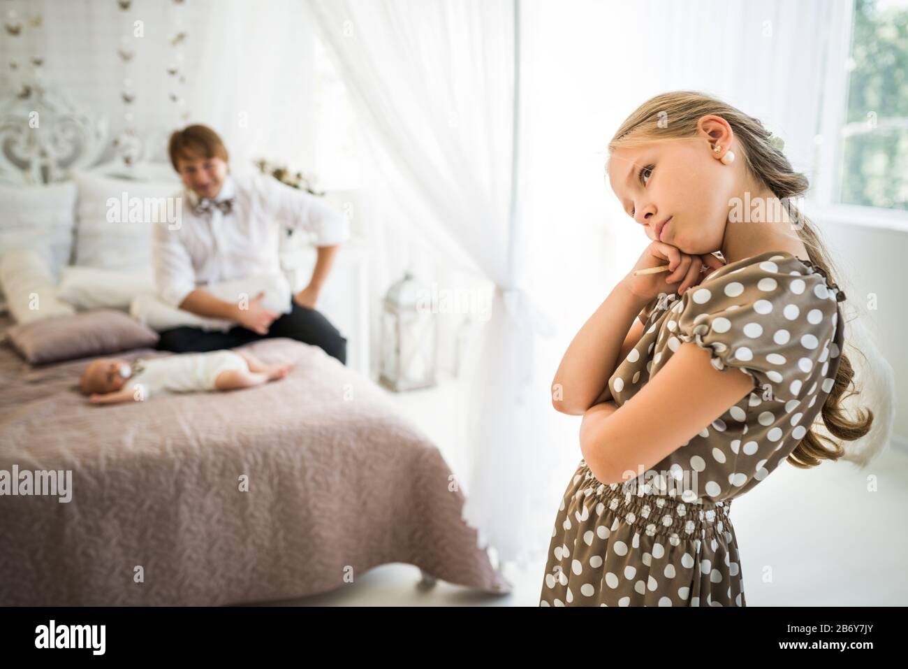 Petite fille mignonne est jalouse de son frère nouveau-né allongé sur le lit à côté des parents heureux floues. Concept d'égoïsme et la grande différence dans Banque D'Images