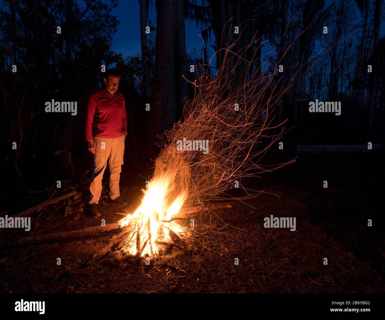 Un homme debout devant un feu de camp la nuit dans la forêt. Banque D'Images