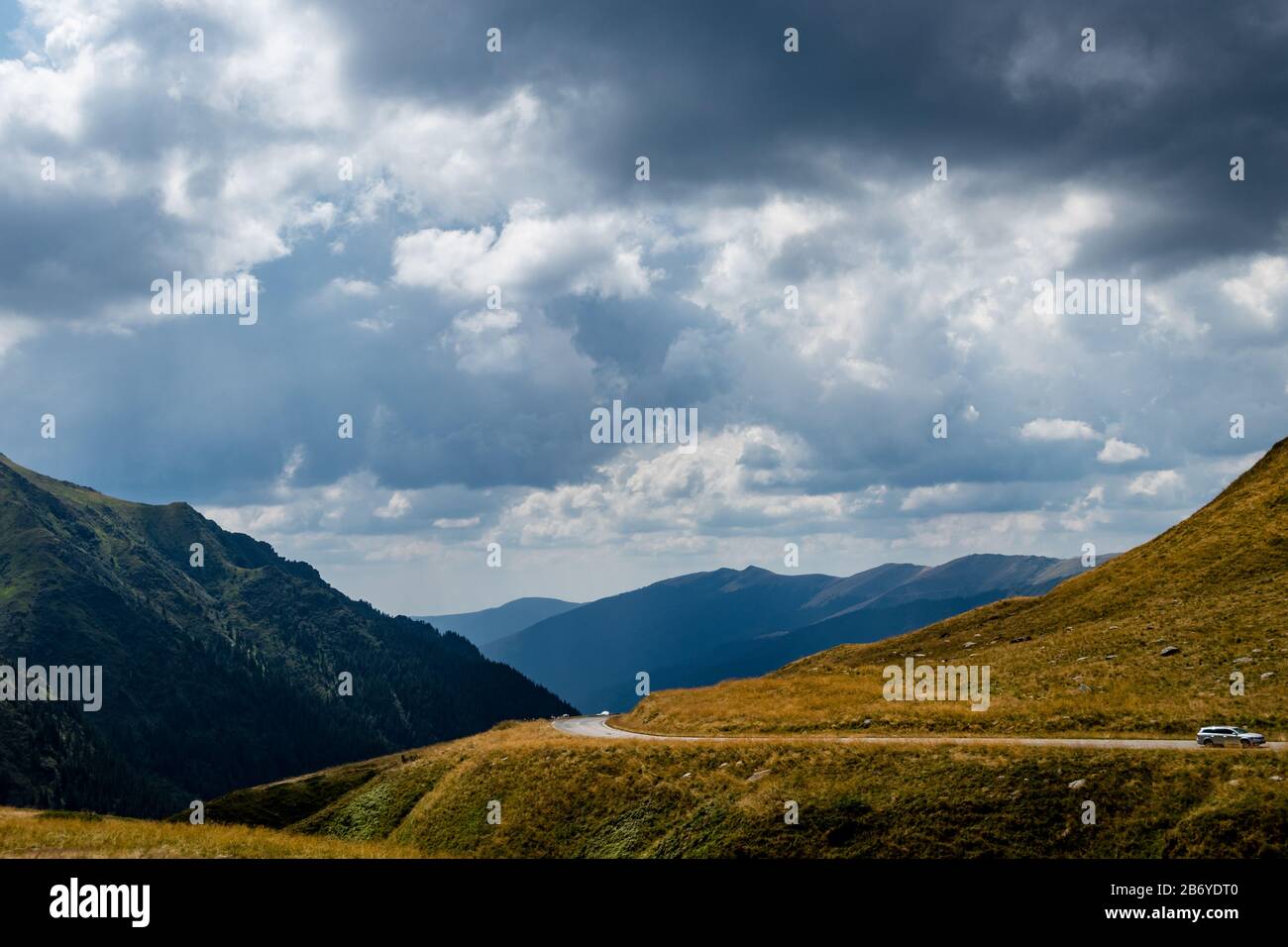 Voiture passant sur la route de montagne avec des montagnes en arrière-plan et des nuages sombres au-dessus Banque D'Images