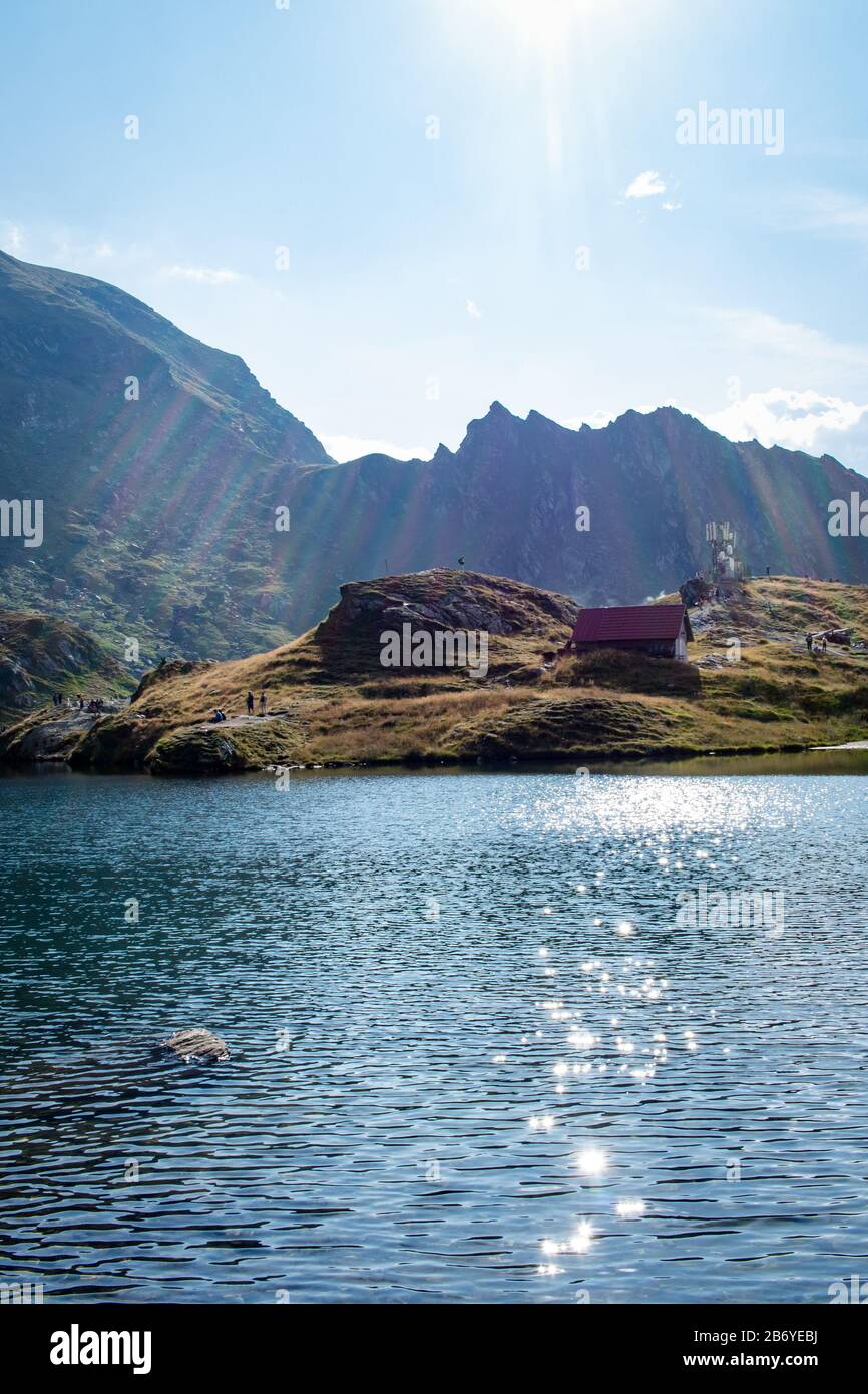 Soleil coulage des rayons sur un lac de montagne avec chalet de montagne et montagne en arrière-plan et nuages puffy au-dessus Banque D'Images