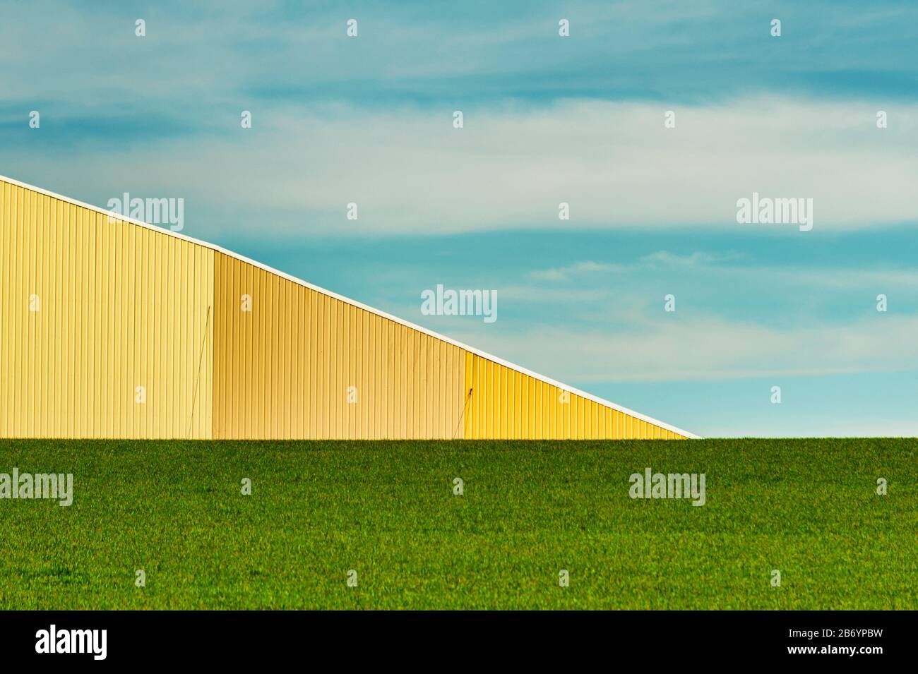 Agriculture minimaliste abstrait d'une cave en métal jaune, champ vert de printemps et ciel bleu avec nuages clairs. Banque D'Images