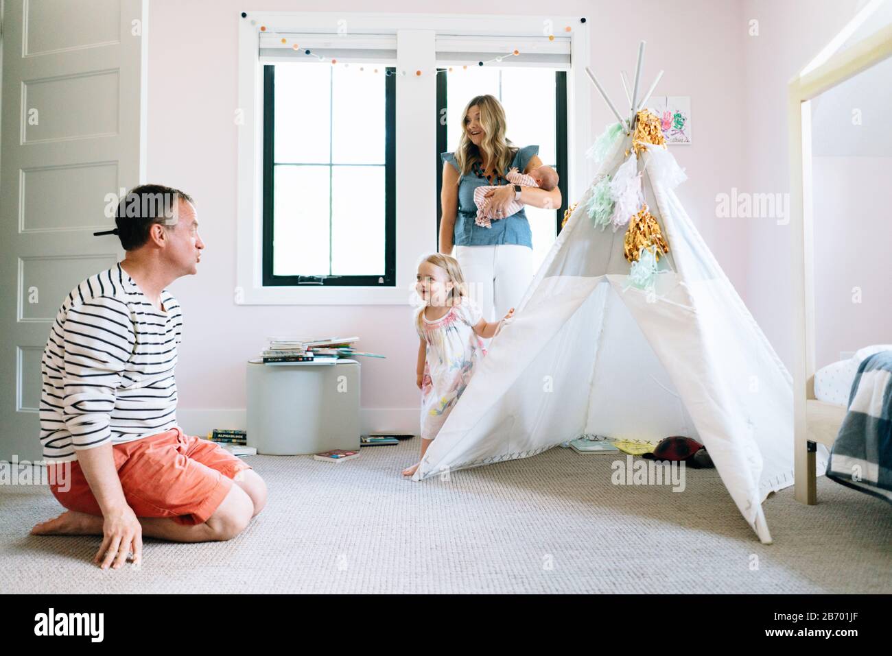 Une famille de quatre personnes joue ensemble dans une chambre d'enfant avec un tipi moderne Banque D'Images