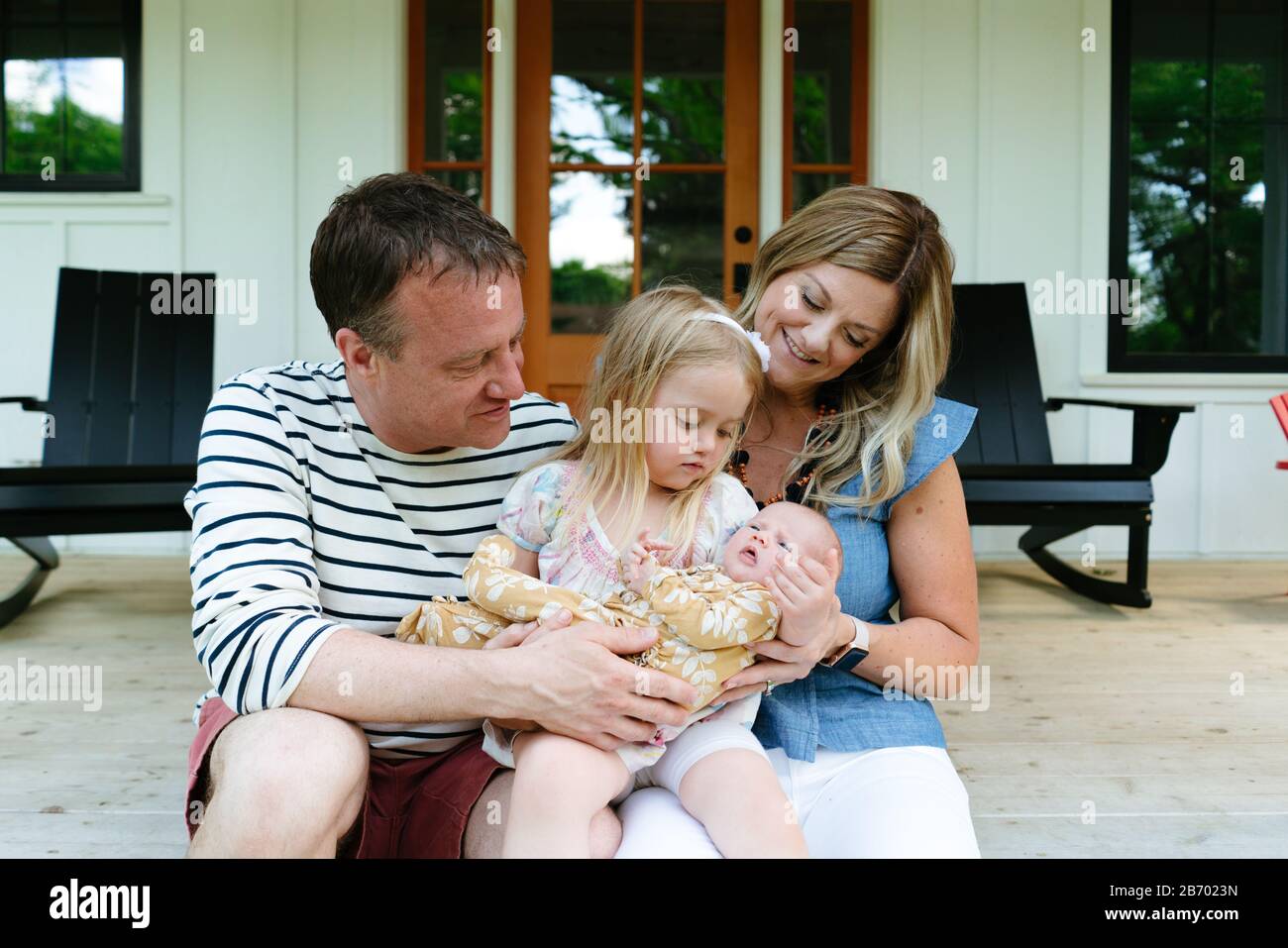 Une jeune fille tient sa petite sœur avec ses parents sur un porche Banque D'Images