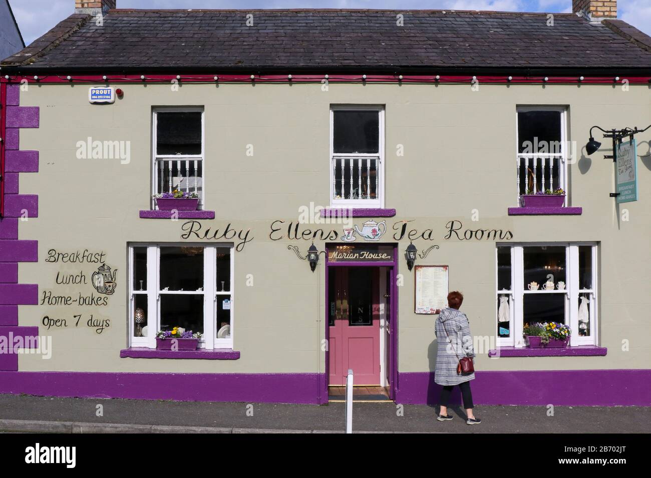 Une femme qui lit un menu et une liste de prix à l'extérieur du Ruby Ellen's Tea Rooms lors d'une journée de printemps ensoleillée avec un ciel bleu à Newry Street, Carlingford, County Louth. Banque D'Images