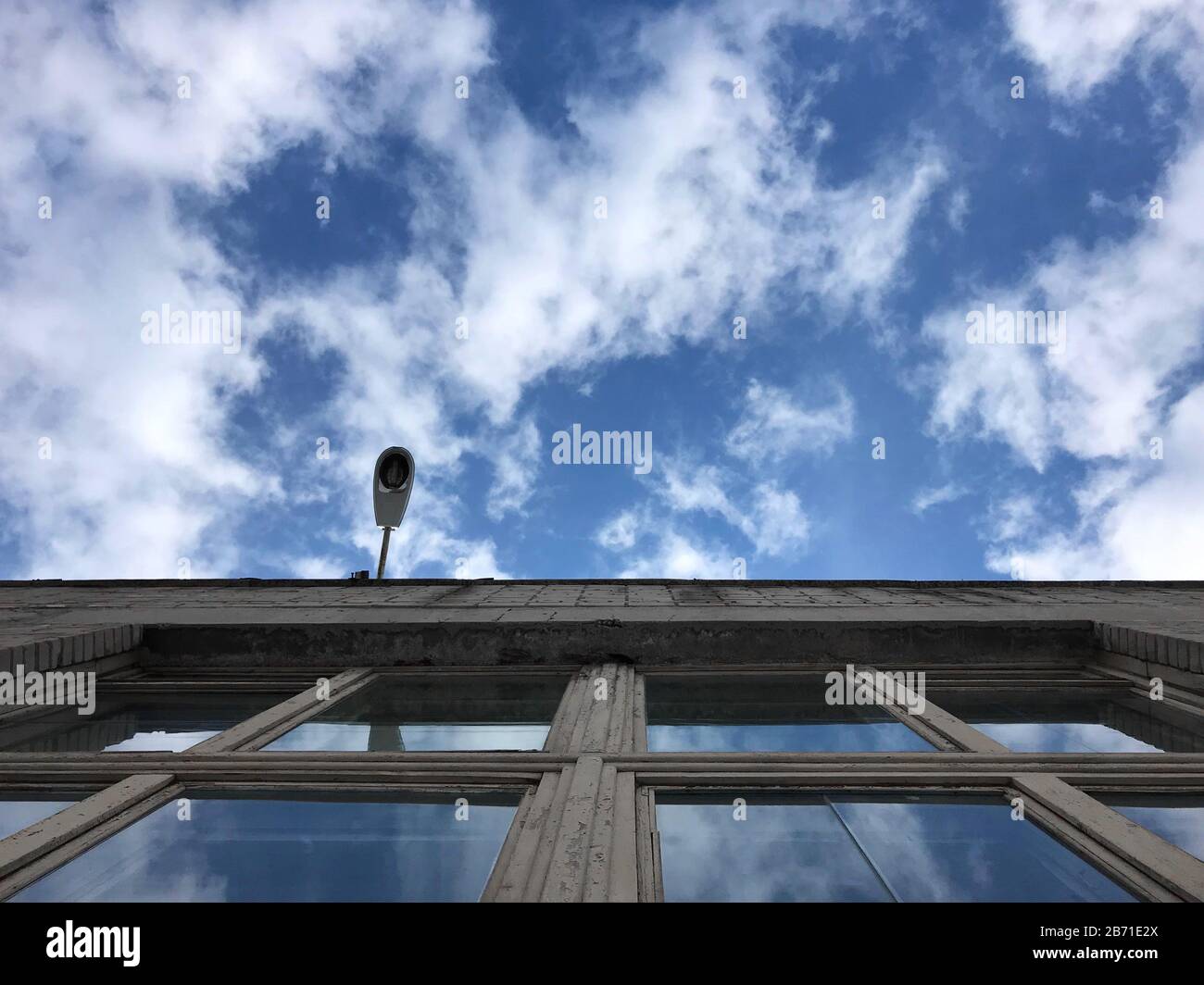 Lampadaire suspendu au mur du bâtiment contre le ciel bleu, le ciel se reflète dans les fenêtres Banque D'Images