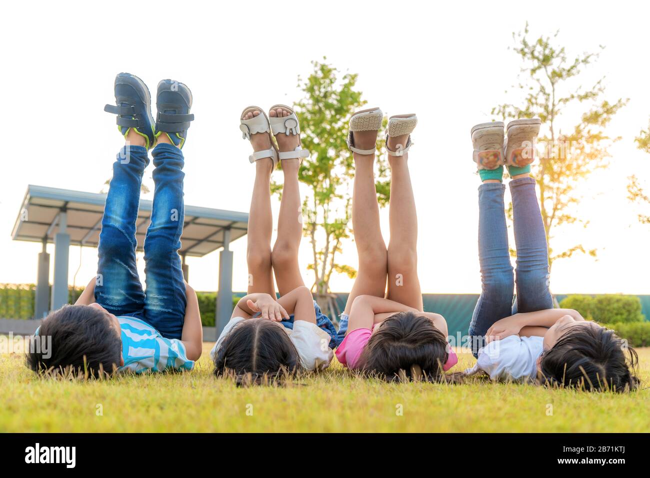 Grand groupe d'heureux amis asiatiques souriants de jardin d'enfants de maternelle sur l'herbe et a levé la jambe dans le ciel ensemble dans le parc sur l'herbe verte sur des s ensoleillés Banque D'Images