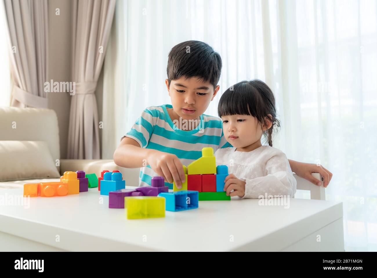 Un joli frère asiatique et sa sœur jouent avec un concepteur de blocs de jouets sur la table dans le salon à la maison. Concept de liaison de frère, d'amitié et d'apprentissage Banque D'Images