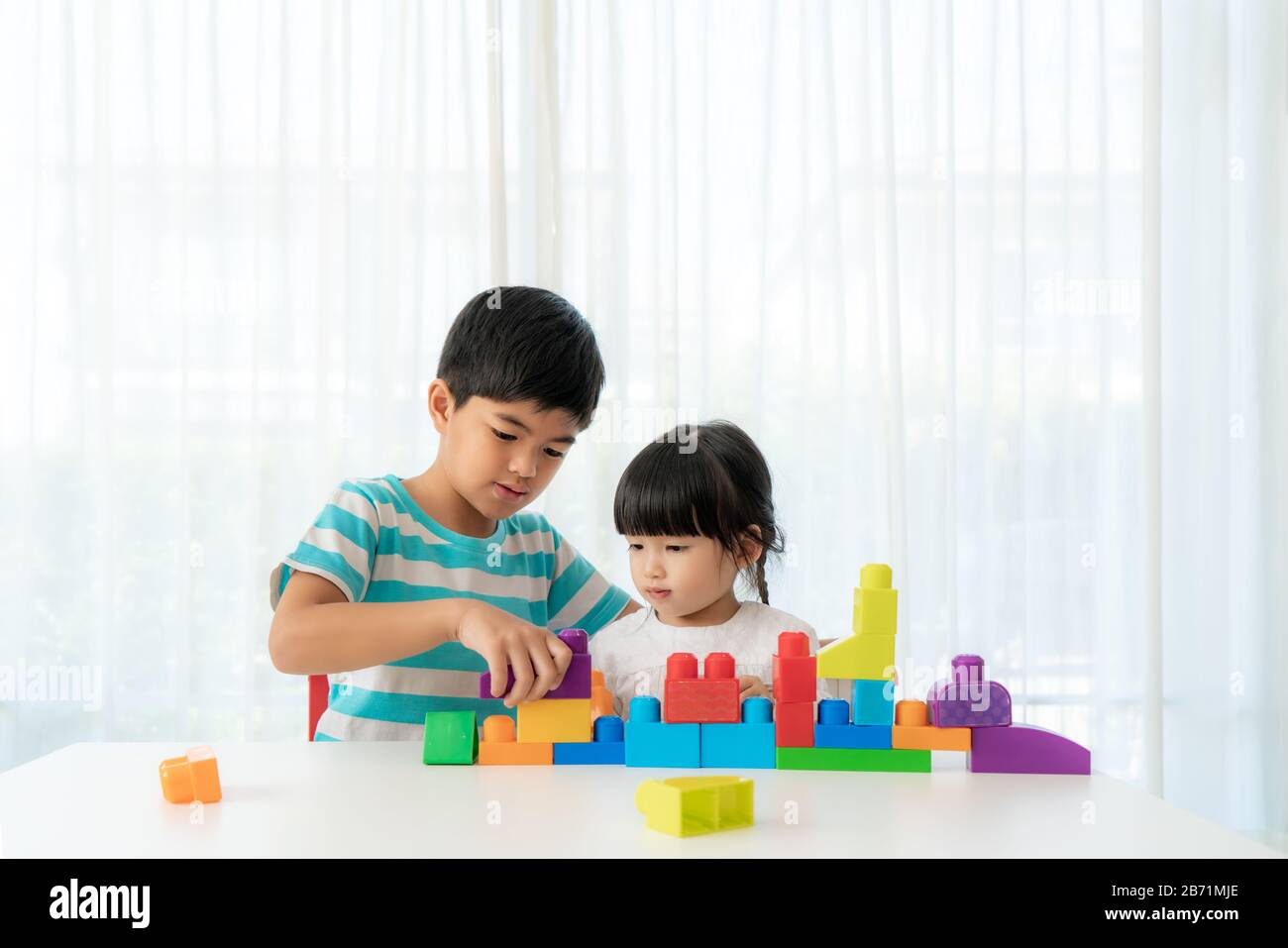 Un joli frère asiatique et sa sœur jouent avec un concepteur de blocs de jouets sur la table dans le salon à la maison. Concept de liaison de frère, d'amitié et d'apprentissage Banque D'Images
