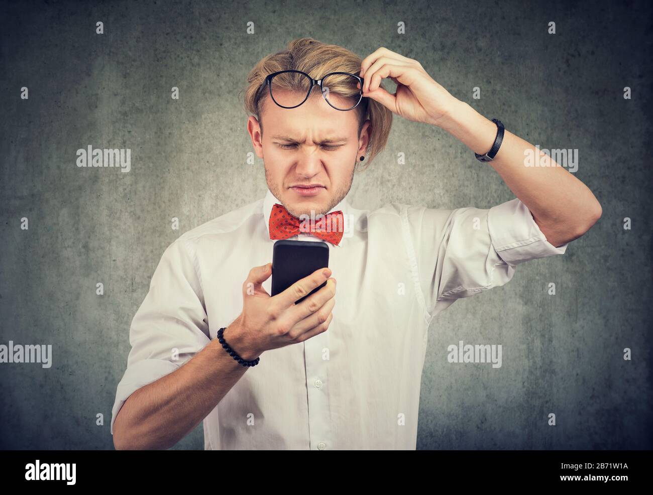 Jeune homme avec des lunettes utilisant le téléphone mobile pour avoir un problème de vision Banque D'Images