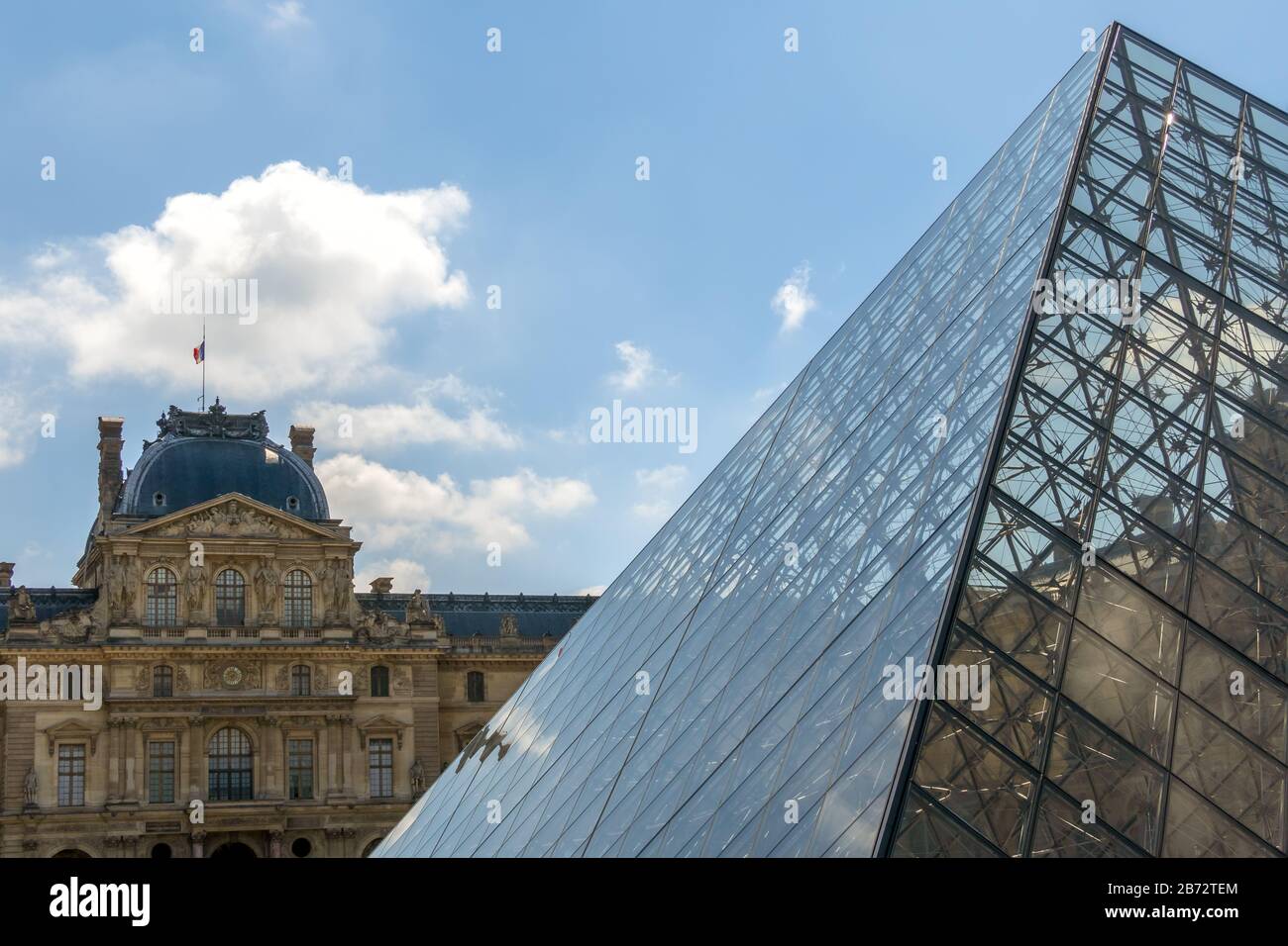 France. Journée ensoleillée dans la cour parisienne du Musée du Louvre. Ancienne façade et pyramide moderne en verre Banque D'Images
