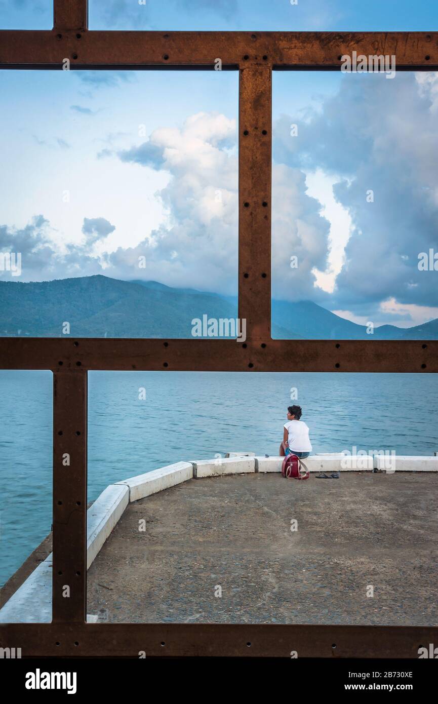 Une vue d'une fenêtre caractéristique sur le quai de Cairns comme une seule touriste féminine prend le temps d'absorber l'atmosphère de vacances. Banque D'Images