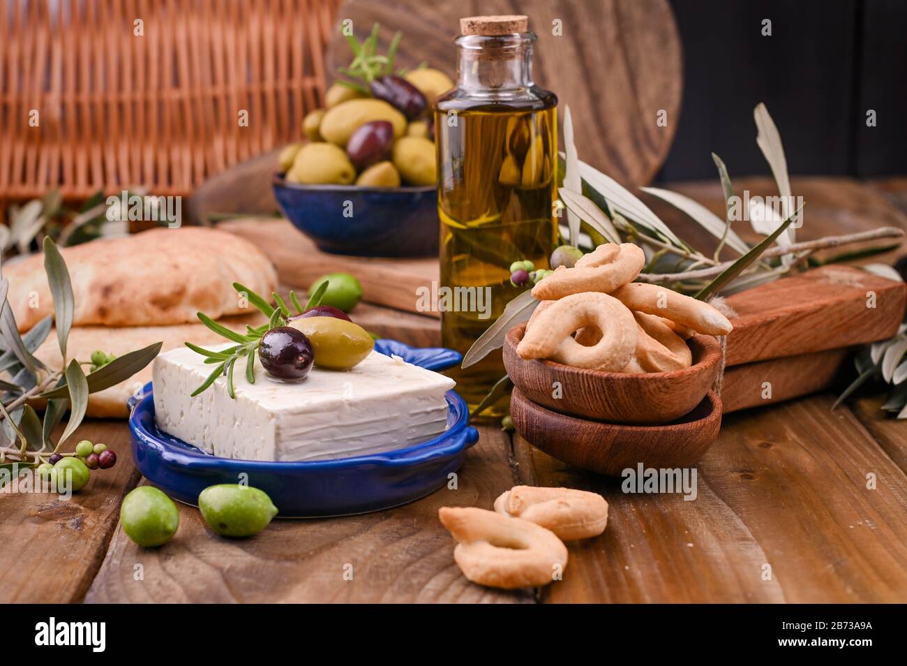 Fromage grec aux olives et CRAQUELINS italiens et ITALIENS ou TARALLI . Branches d'olive fraîches, huile d'olive dans une bouteille avec des collations italiennes traditionnelles. Espace de copie Banque D'Images
