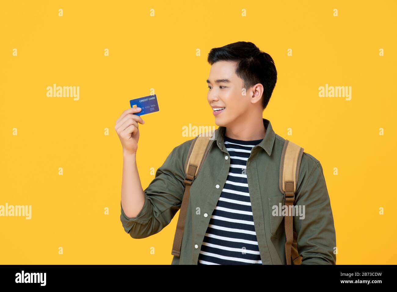Un jeune touriste asiatique muni d'une carte de crédit prêt à voyager isolé sur fond jaune Banque D'Images