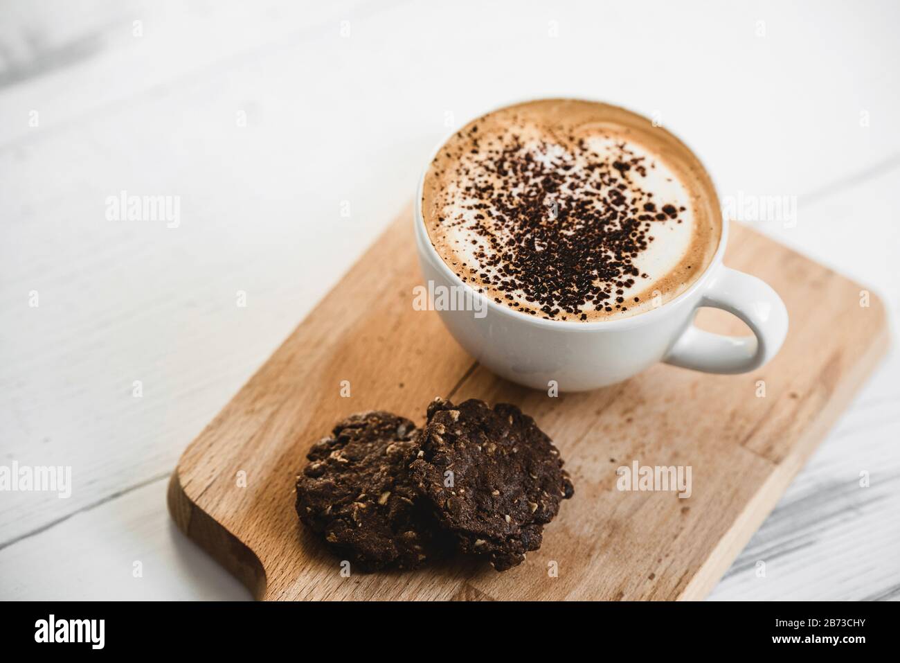 Café au lait chaud dans la tasse avec biscuits au chocolat sur une assiette de bois dans le café pour le petit déjeuner Banque D'Images