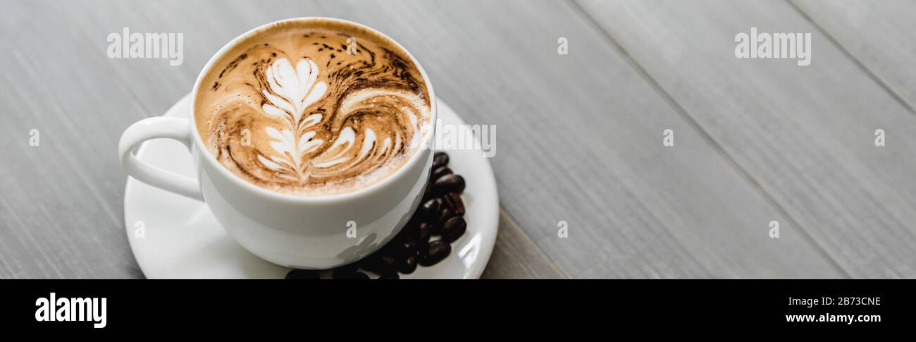 Café fraîchement préparé avec de l'art de latte à motif fern dans une tasse blanche sur fond de bannière en bois Banque D'Images