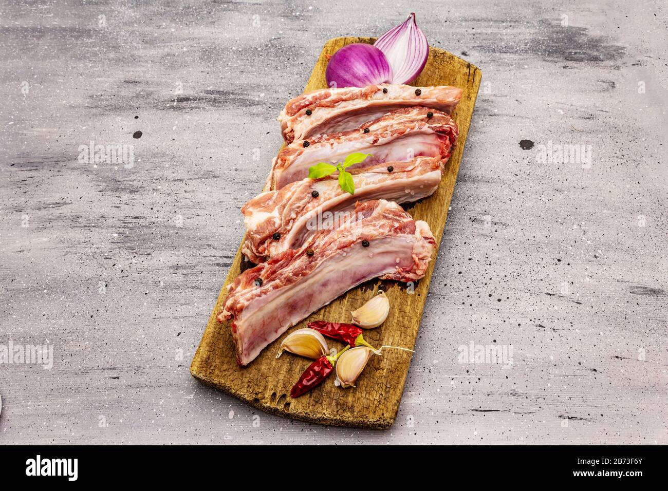 Côtes de porc brutes sur fond de béton gris. Planche à découper ronde en bois, légumes, épices et légumes verts Banque D'Images