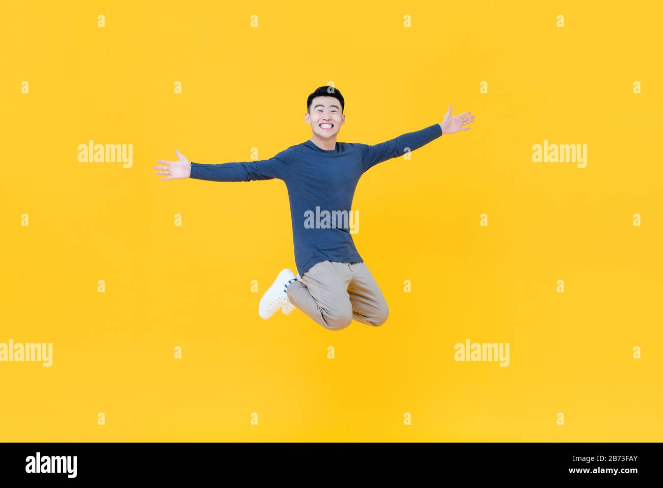 Corps entier de jeune homme asiatique dynamique souriant et sautant avec des bras démesurés isolés sur fond jaune Banque D'Images