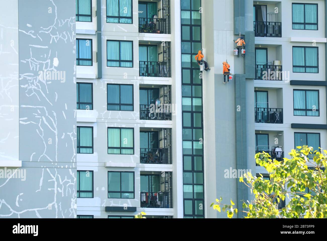 Trois travailleurs de l'accès à la corde peignant la façade d'un bâtiment moderne élevé Banque D'Images