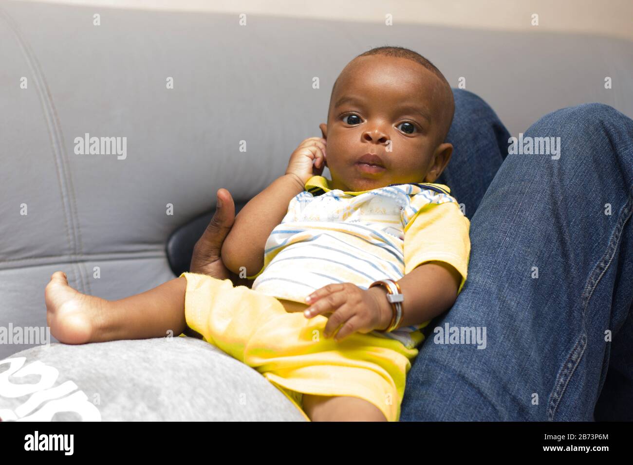 bébé nouveau-né allongé sur les jambes de son père dans le canapé à la maison regardant la caméra. Banque D'Images
