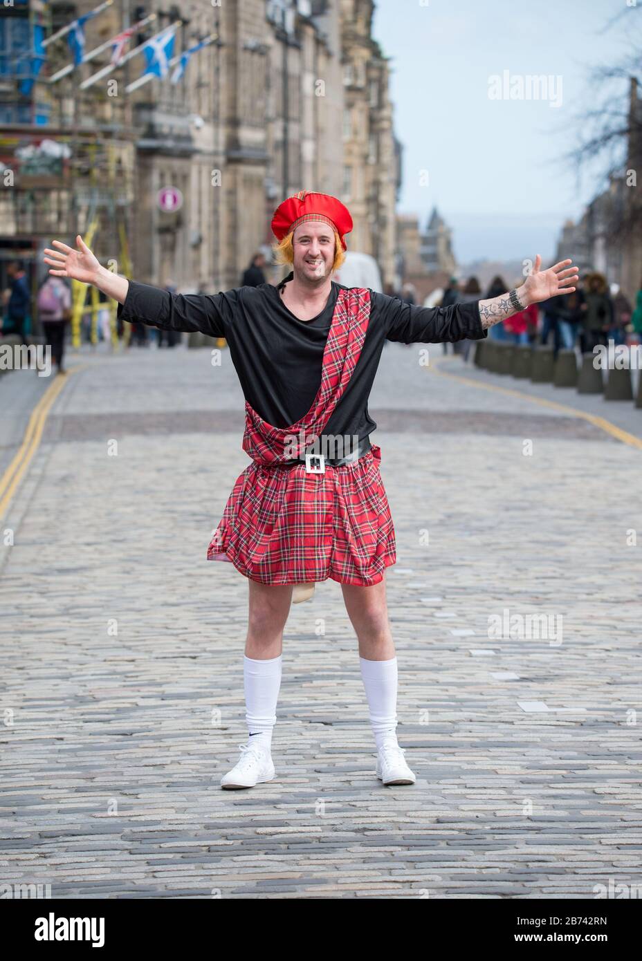 Édimbourg, Royaume-Uni. 13 mars 2020. Photo: Homme vu sur le Royal Mile à  Edimbourg portant un kilt de tartan, le écossais plaid et le chapeau rouge,  en stretant ses trucs pour la