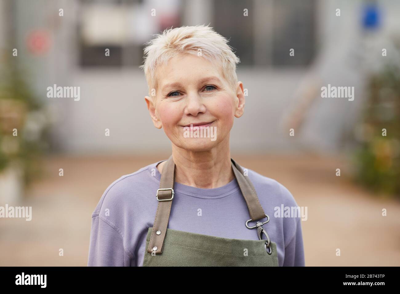 Portrait d'une femme mûre avec des cheveux blonds courts regardant l'appareil photo tout en travaillant comme jardinier Banque D'Images