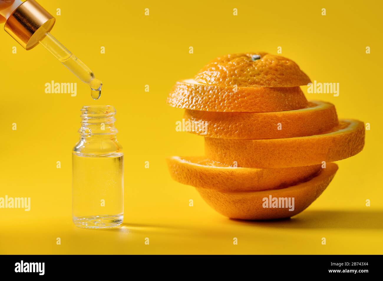 flacon d'extrait d'agrumes avec compte-gouttes et tranches d'orange sur fond jaune Banque D'Images