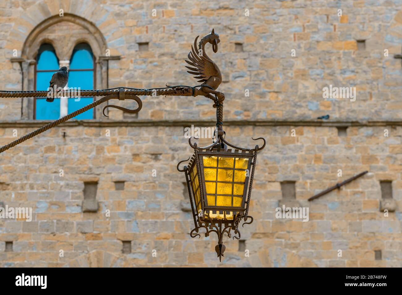 Une lampe de rue en verre ornée, tenue par une créature mythique en métal dans la vieille ville historique de Volterra, Toscane, Italie. Banque D'Images