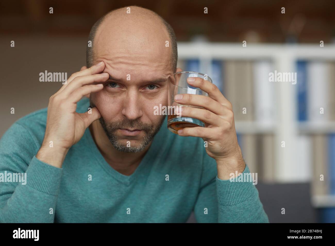 Portrait de l'homme ivre mûr tenant le verre avec le whisky et regardant l'appareil photo avec une vue triste Banque D'Images