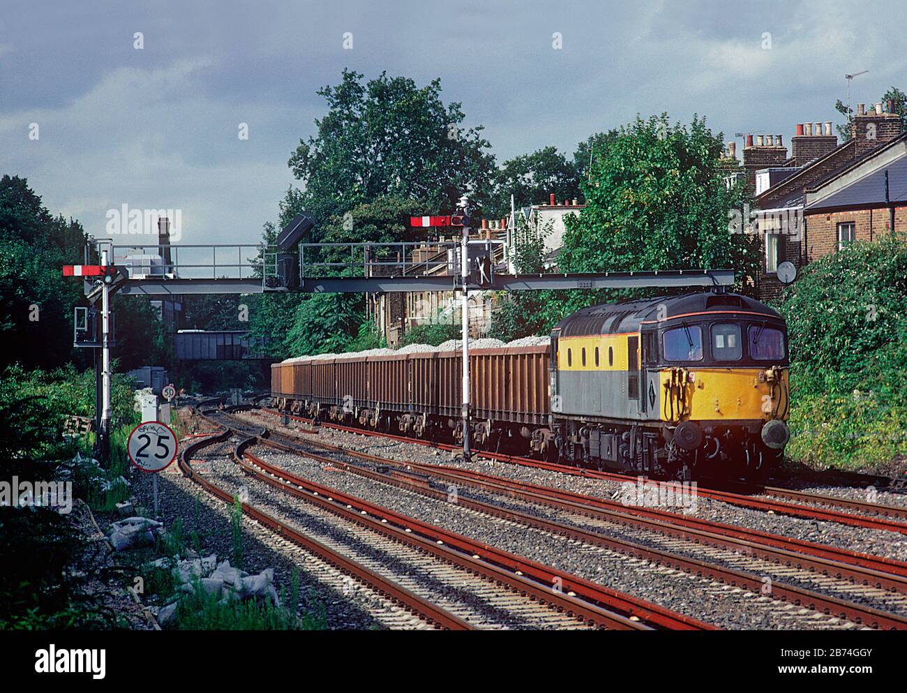 Une locomotive diesel de classe 33 numéro 33118 qui travaille un train de wagons de ballast chargés à côté de certains signaux de sémaphore à Kensington Olympia dans l'ouest de Londres. Banque D'Images