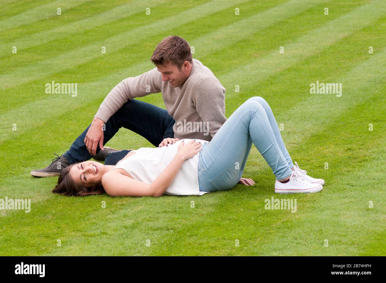 Belle jeune femme enceinte posée sur l'herbe avec son partenaire assis à côté d'elle Banque D'Images