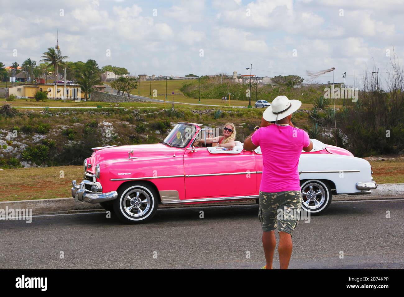 La Havane, Cuba - chauffeur de taxi photographiant les touristes sur son Chevrolet rose classique Banque D'Images