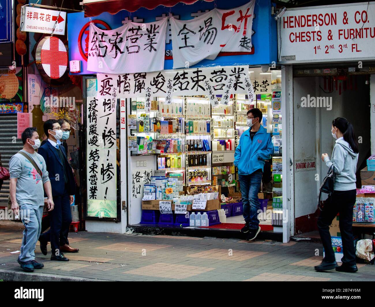 Les gens marchent devant un magasin qui lit:'Mal Grave par Coronavirus, sera hors des affaires" à Tsim Sha Tsui de Hong Kong. Banque D'Images