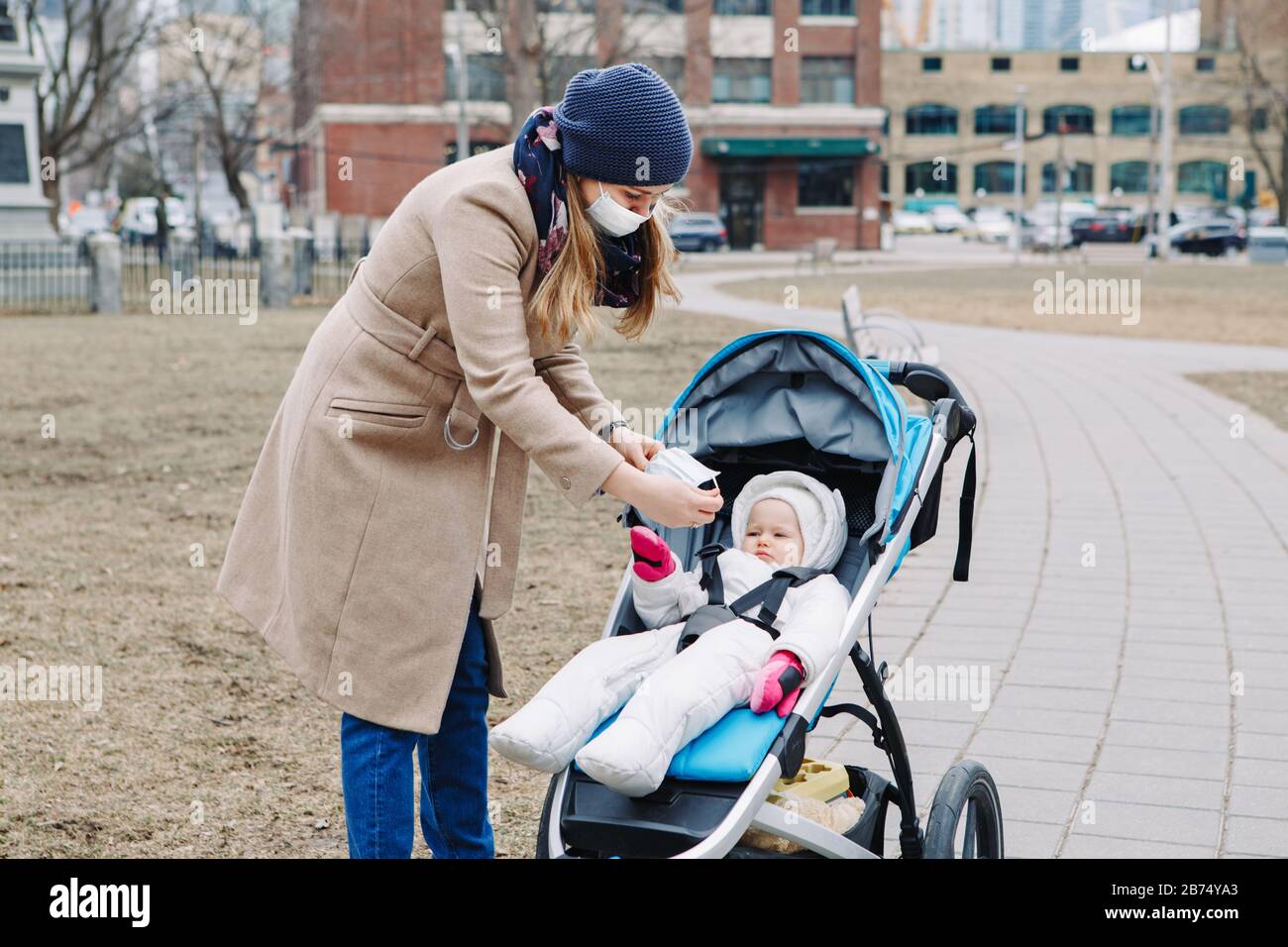 Une jeune mère caucasienne a mis un masque chirurgical sur le bébé extérieur à Toronto. Masque protecteur précaution contre la nouvelle pneumonie atypique chinoise COVID-1 Banque D'Images