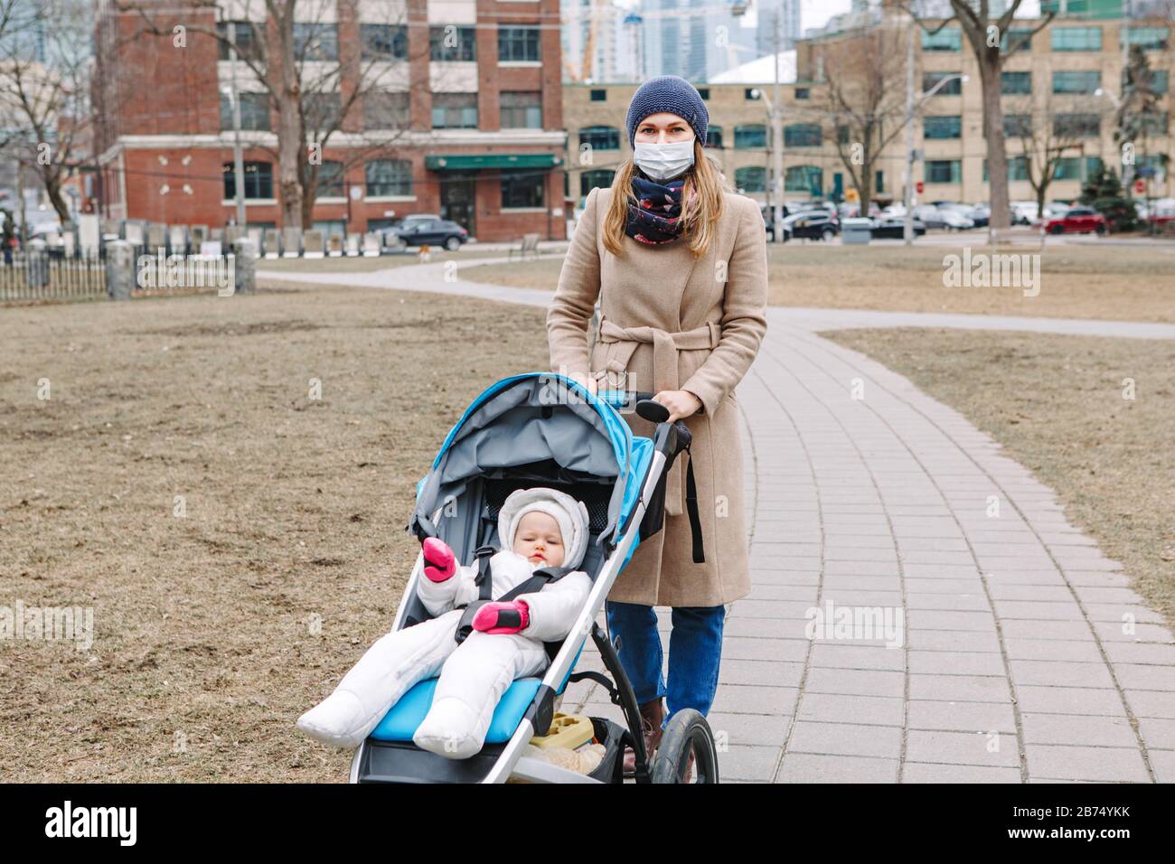 Jeune mère caucasienne en masque chirurgical marchant avec bébé en plein air à Toronto. Masque protecteur précaution contre la nouvelle pneumonie atypique chinoise C Banque D'Images