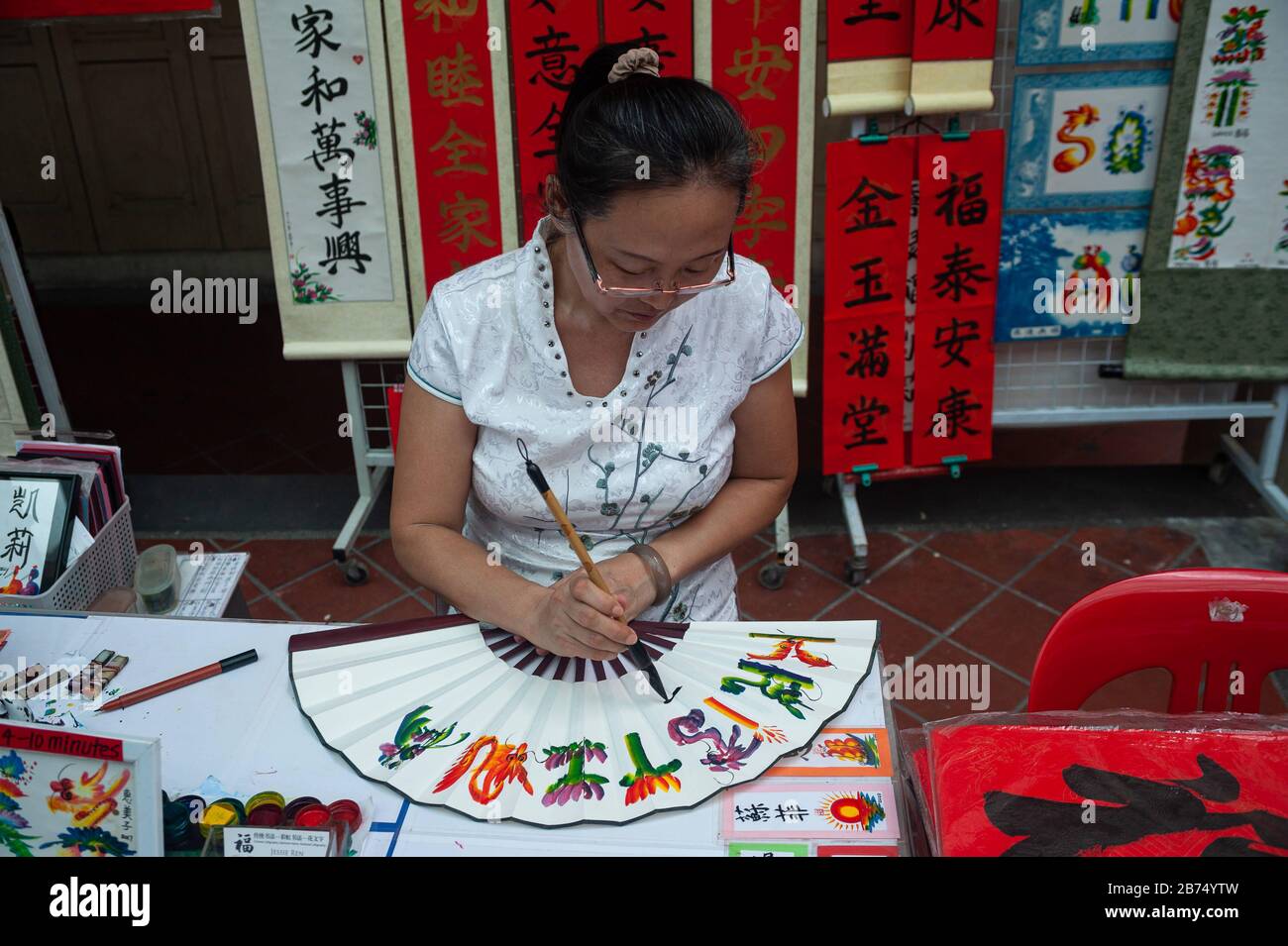 17.01.2020, Singapour, République de Singapour, Asie - l'artiste Jessie Ren écrit des fans, des bannières et des rouleaux avec des félicitations et des bénédictions individuelles pour le nouvel an chinois à venir sous la forme de calligraphie chinoise peignée à la main dans un stand de rue dans le quartier de Chinatown. [traduction automatique] Banque D'Images