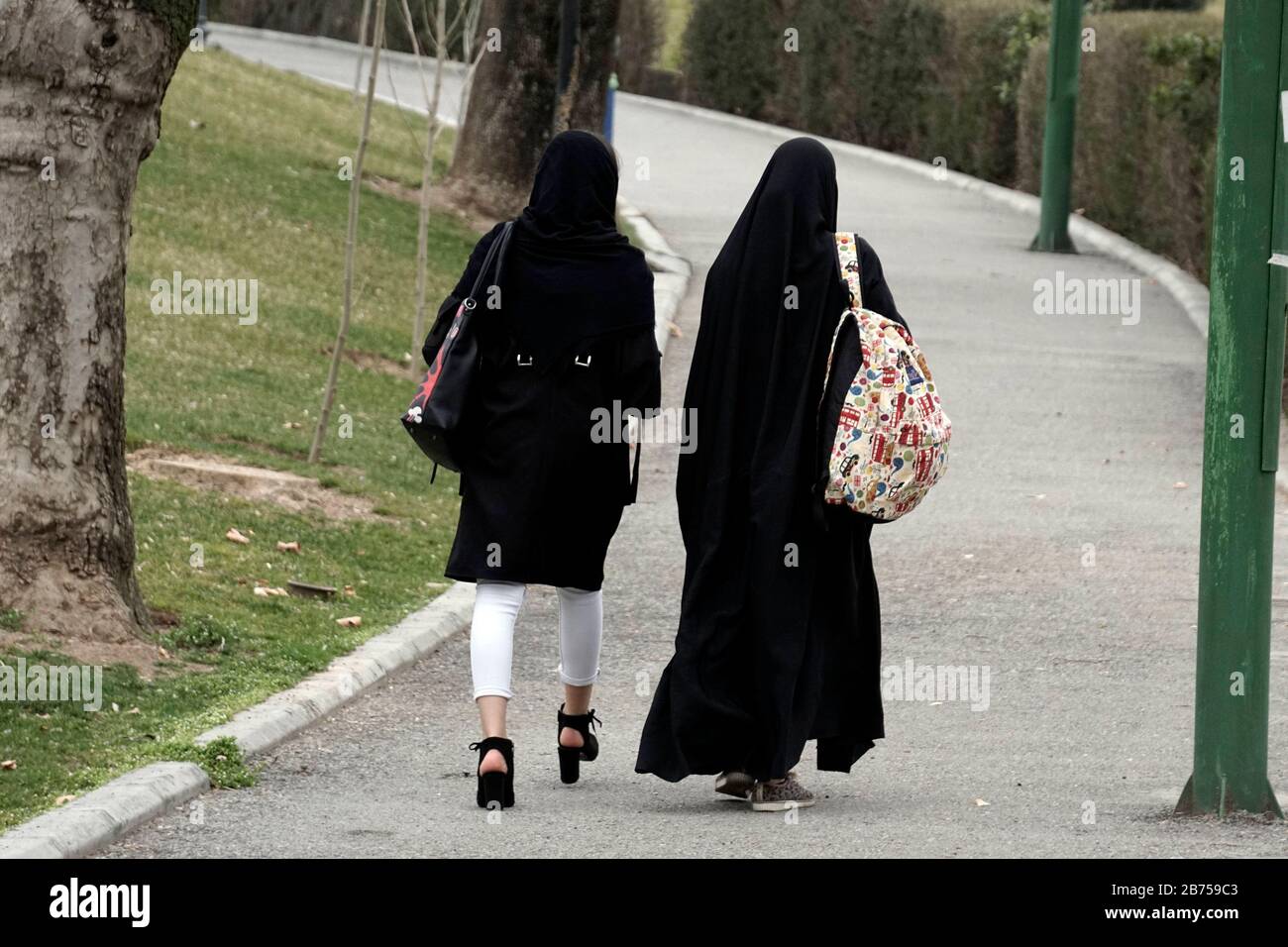 Une femme avec des chaussures à talons hauts et une femme avec un chador  marchent dans un parc à Téhéran, en Iran, le 14.03.2019. Une fois que les  États-Unis se sont retirés