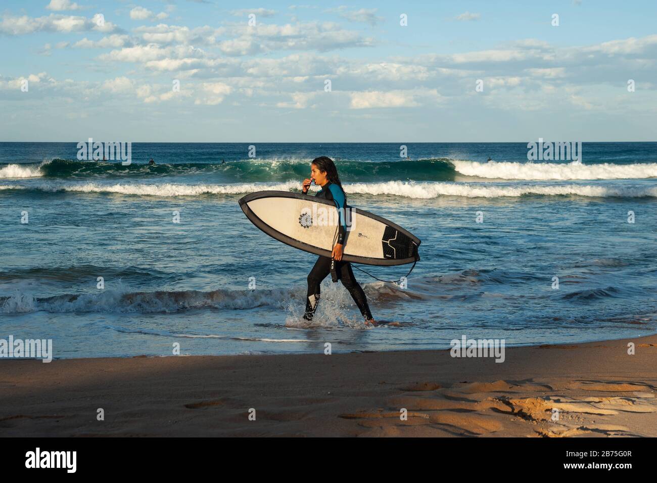 10.05.2018, Sydney, Nouvelle-Galles du Sud, Australie - une femme marche le long de Manly Beach avec son planche de surf sous son bras, tandis que d'autres surfeurs attendent en arrière-plan la bonne vague. [traduction automatique] Banque D'Images