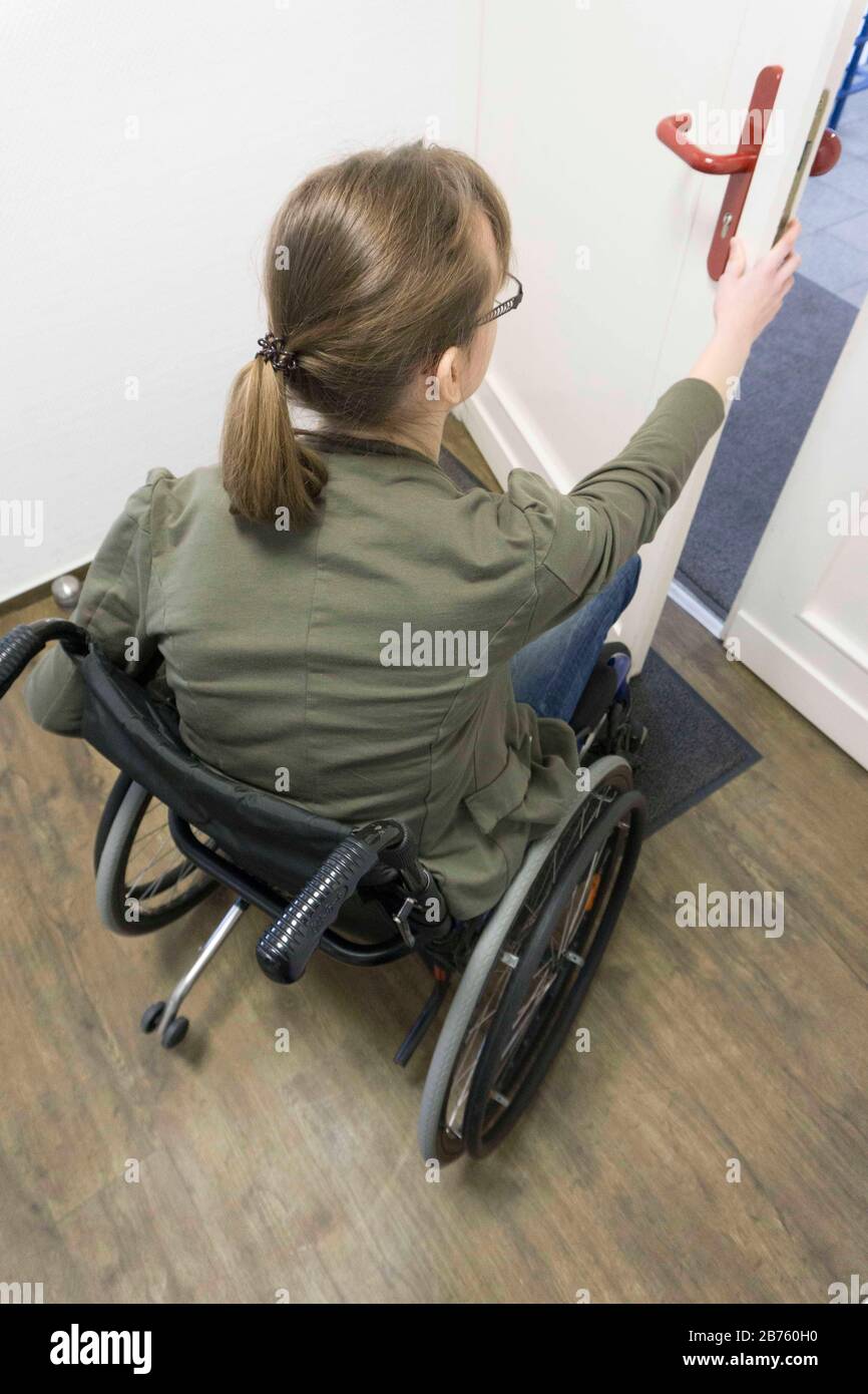 Une jeune femme handicapée en fauteuil roulant ouvre une porte d'entrée le  18.01.2017. Souvent, les portes des bâtiments publics ne sont pas adaptées  aux personnes handicapées, parce qu'elles n'ont pas de largeur