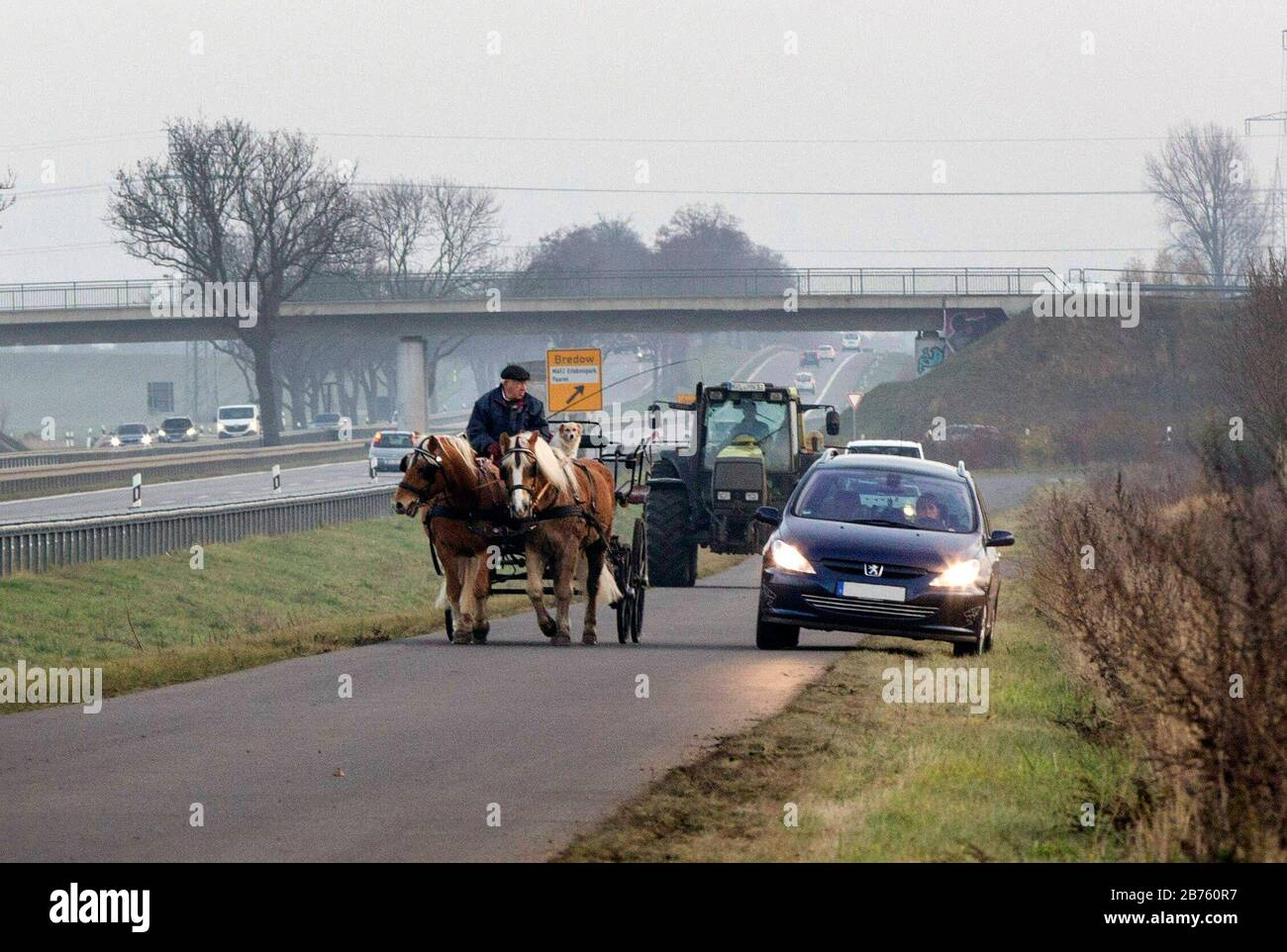 Un coachman conduit son chariot sur une route très fréquentée et est dépassé par un conducteur de voiture. [traduction automatique] Banque D'Images