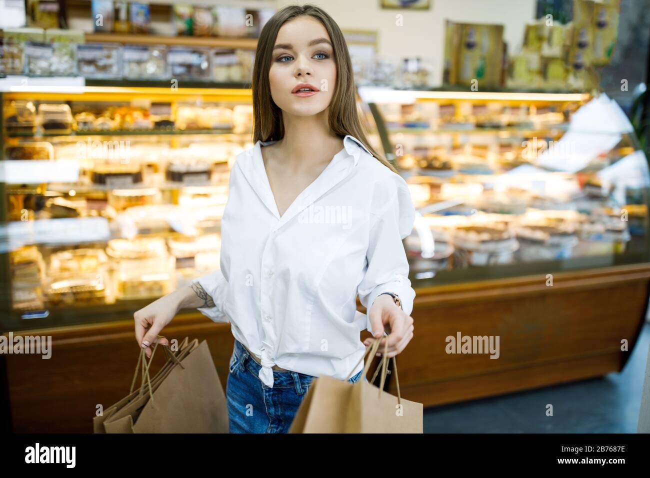 Une jeune femme tient des sacs en papier dans ses mains et se tient près d'une vitrine de magasin avec des bonbons Banque D'Images
