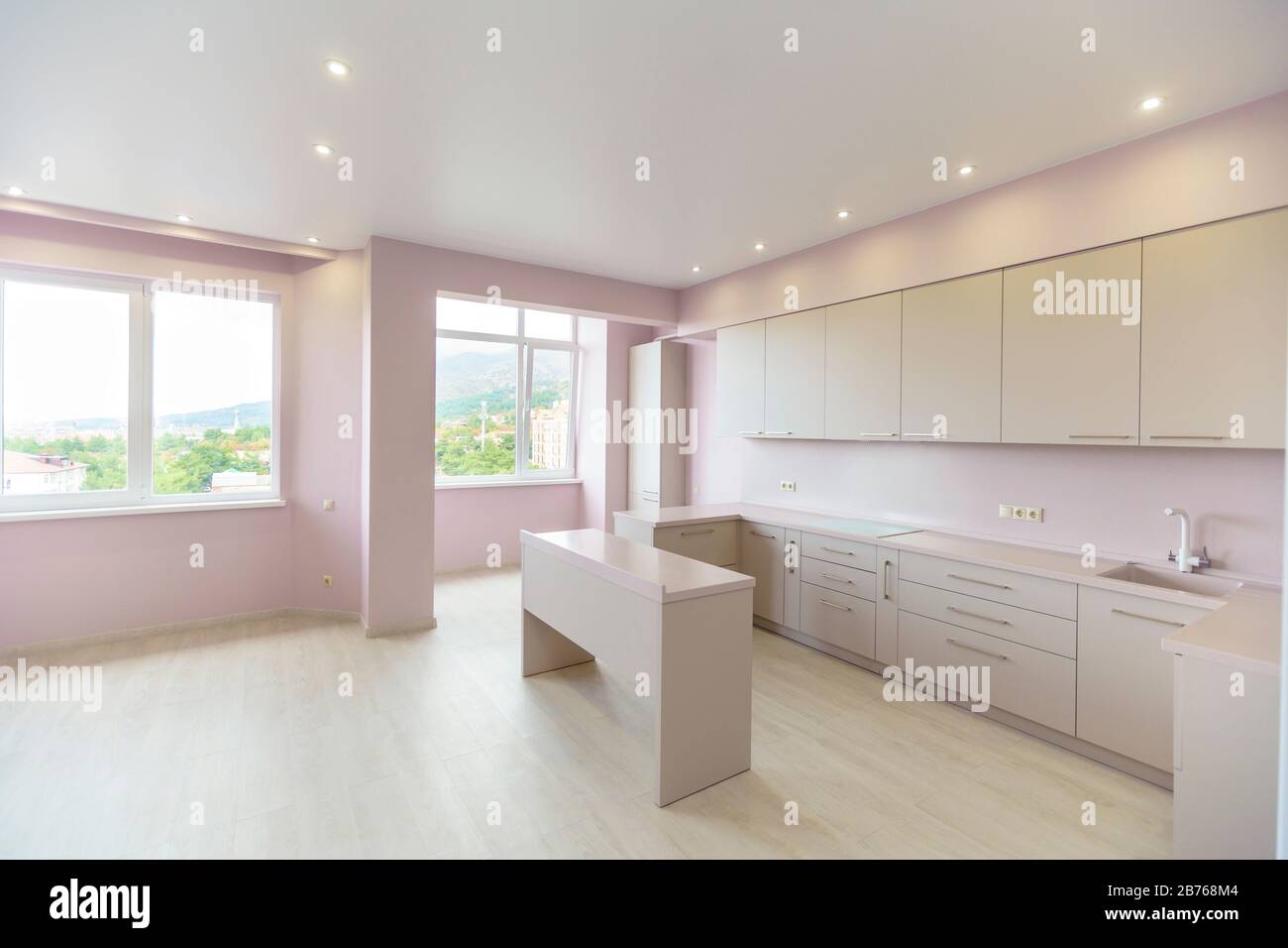 Une grande chambre avec des murs roses et un ensemble de cuisine blanche. Le mobilier de cuisine est neuf avec tous les appareils de cuisine. Devant la cuisine se trouve une table blanche. Banque D'Images