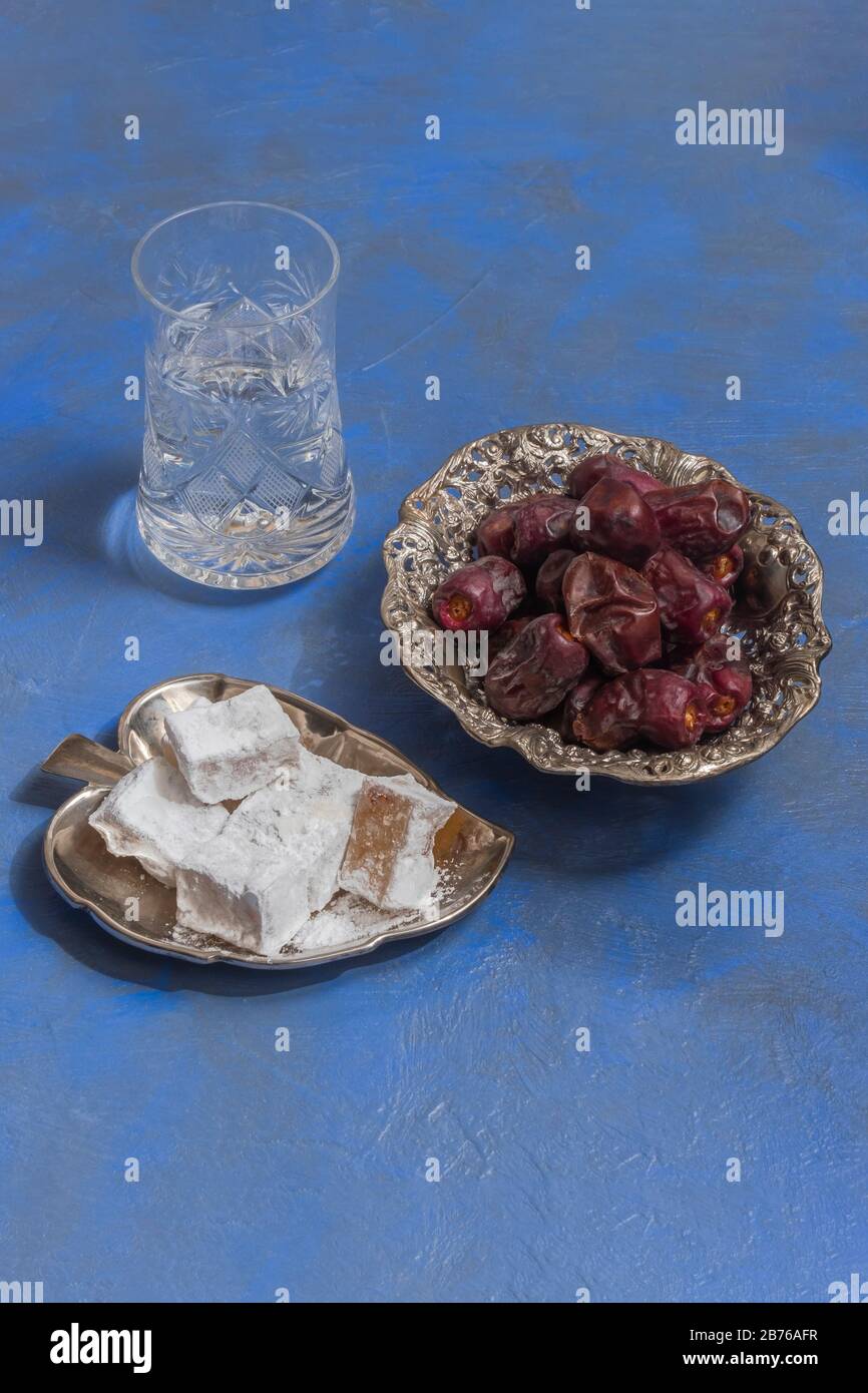 Délectez le lokum avec des dattes sèches et une tasse d'eau sur fond bleu Banque D'Images