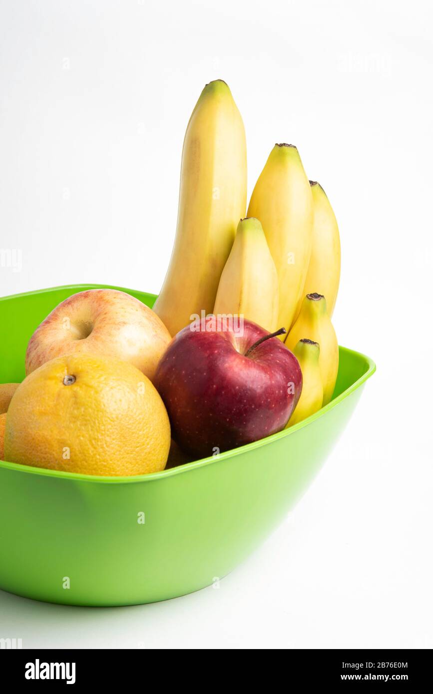 Un bol en plastique vert vif avec des fruits frais et mûrs disposés avec art, tels que des pommes, des bananes, des oranges et d'autres sur un fond blanc Uni. Banque D'Images