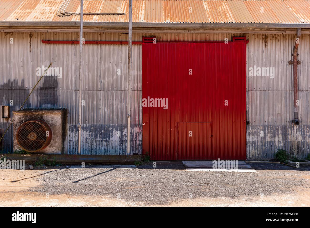 Grange métallique ou porte coulissante de dépôt de couleur rouge avec un vieux ventilateur d'extraction Banque D'Images