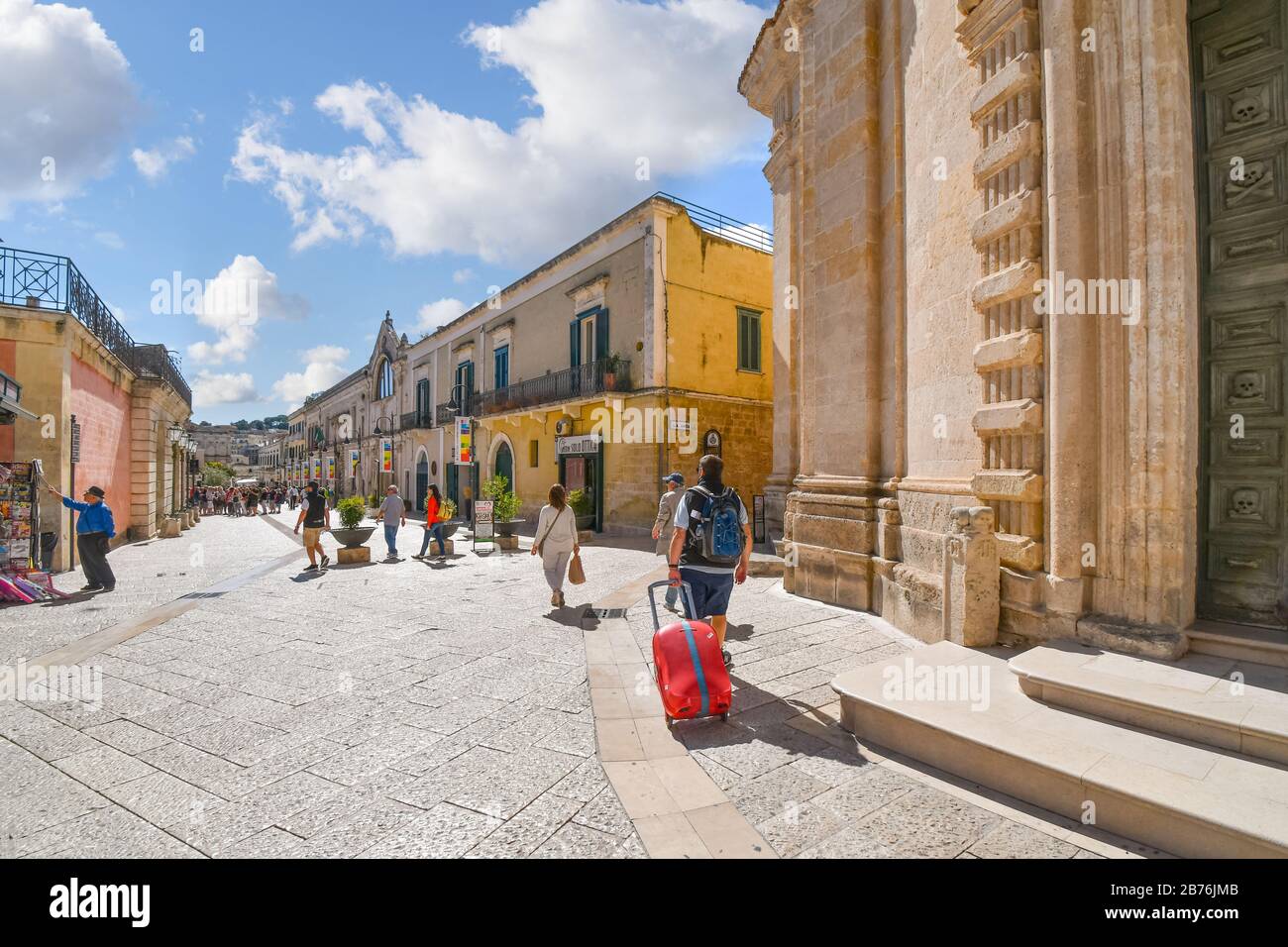Les touristes y compris un homme avec une valise à roulettes passent par l'église du purgatoire de la Piazza Vittorio Veneto dans l'ancienne ville de Matera, Italie. Banque D'Images