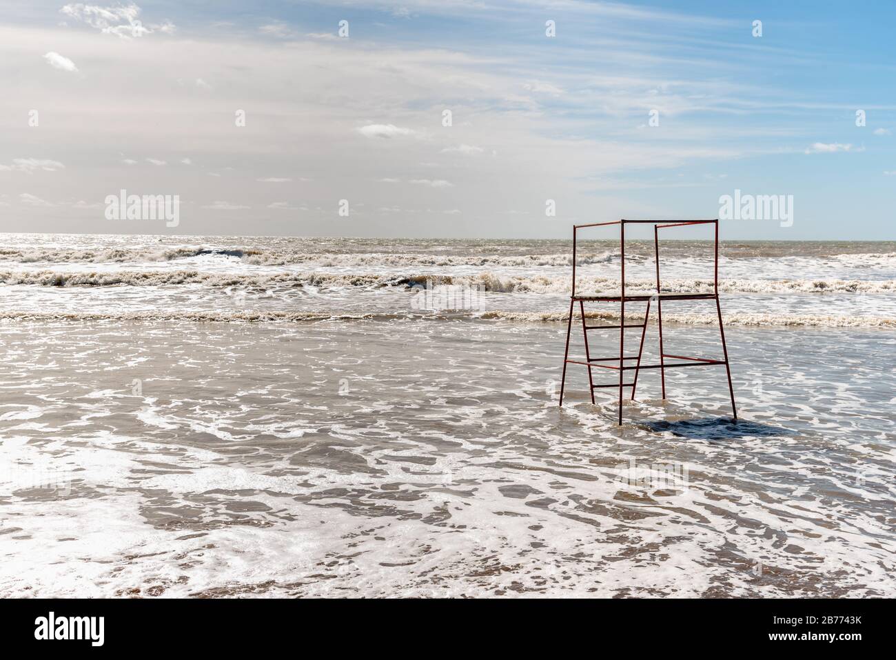 Plage vide en Argentine avec marée haute avec un stand de sauveteur rouge fait de tubes avec quelques nuages Banque D'Images