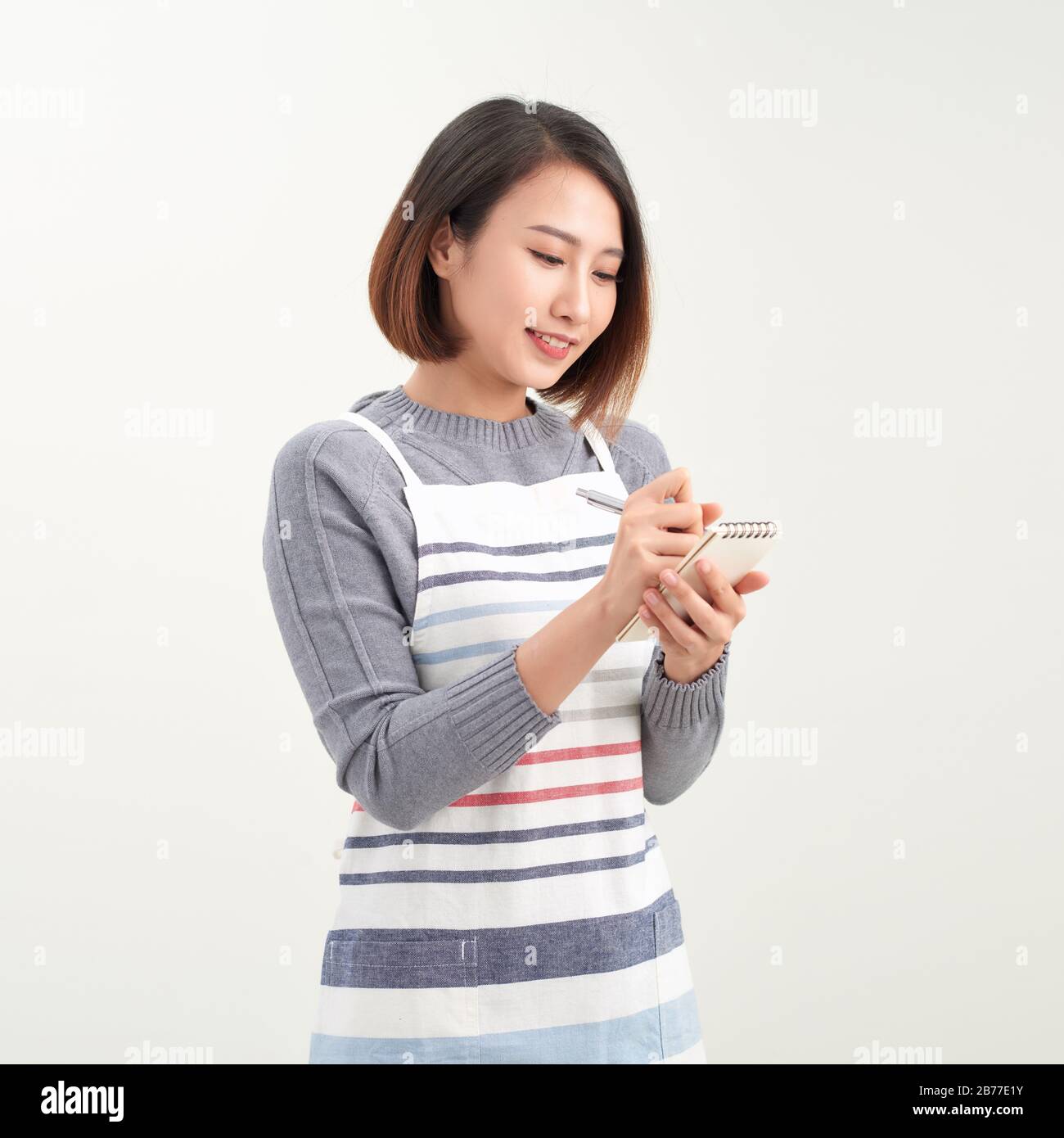 Bonne fille asiatique serveur en tablier écrire la commande et regarder l'appareil photo Banque D'Images