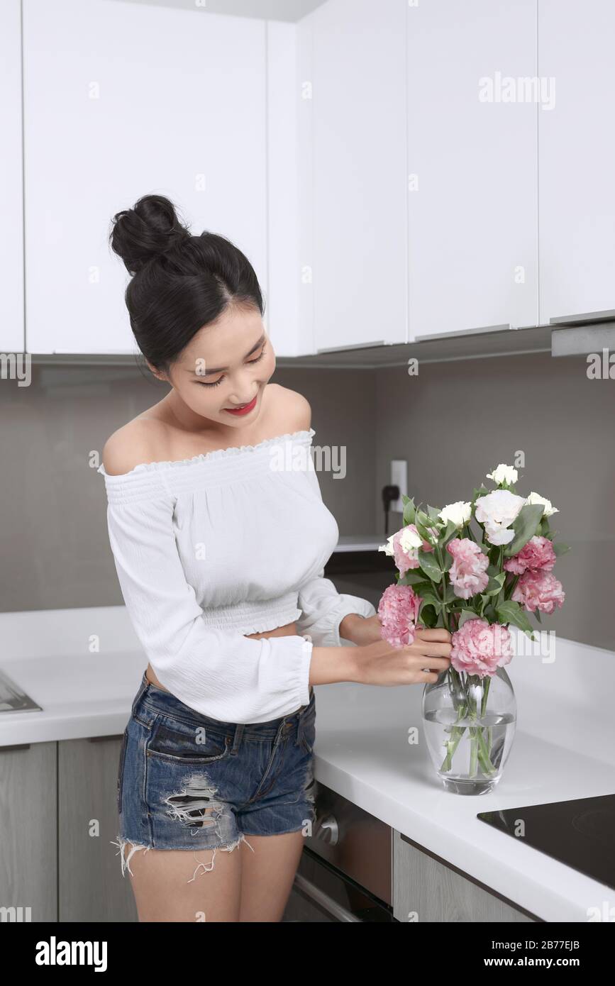 Jeune femme asiatique belle organisant des fleurs dans vase dans la cuisine. Banque D'Images